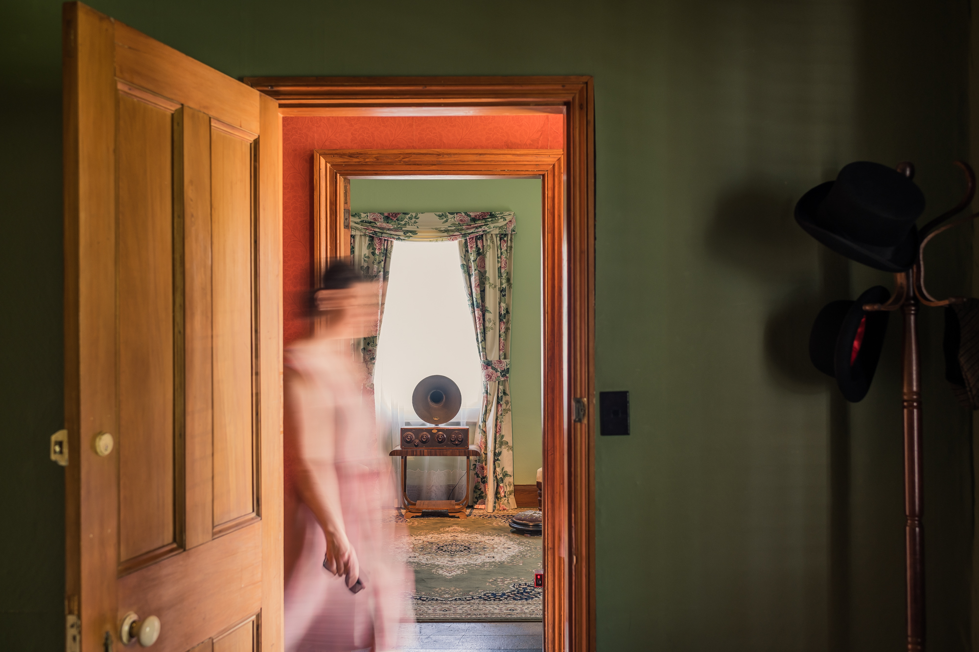 A woman walks along the hallway of Nairn Street Cottage. She is framed by an open bedroom door. She appear blurry with movement.