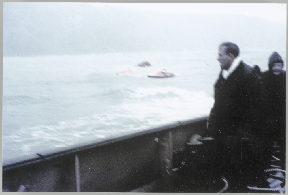 Man on the deck of the TEV Wahine looks out on two red liferafts and a lifeboat